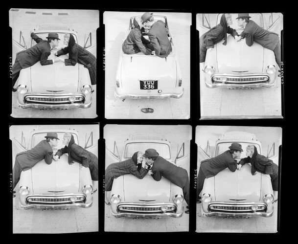 NP_NP05E4_1957_026D: Couple lighting cigarettes over a car, Vogue BW 1957